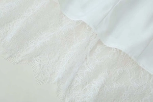 Detailed close-up of white garment hem featuring intricate eyelash lace stitching
