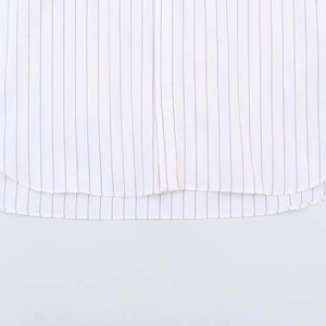 Detail view of the curved hem and red pinstripe pattern on the white cotton shirt