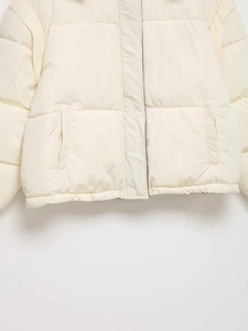 Detail view of cream quilted puffer jacket with slanted pockets and windproof fabric texture