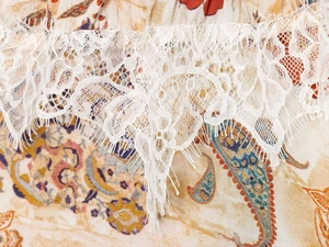Close-up of white eyelash lace trim on a yellow paisley print bohemian dress fabric