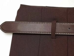 Detail of high waist pleated skirt featuring a brown leather belt with white contrast stitching