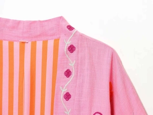 Detail of pink embroidered kaftan jacket with orange striped lining and linen texture