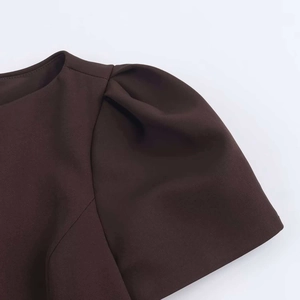 Close-up of crew neckline and puff sleeves with pleat details on dark brown dress