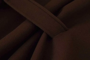 Detailed view of dark brown woolen fabric with fine stitching and crossover belt design