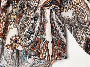 Détail d'un chemisier en mousseline bohème avec motif paisley en orange et bleu marine