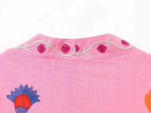 Close-up of pink linen kaftan featuring intricate green vine and floral embroidery detail