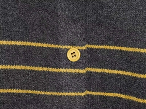 Detail of dark grey knit cardigan showing yellow stripe patterns and a matching round button