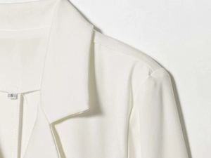 Macro shot of white blazer collar and shoulder detail with woven texture and size S tag