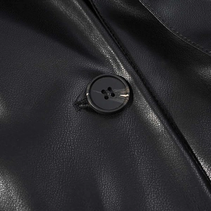 Détail de la texture d'un manteau en cuir noir avec un bouton rond et un grain de cuir