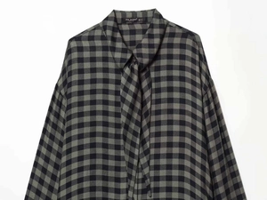 Close-up detail of black and gray plaid shirt fabric with neck ribbon tie and logo tag