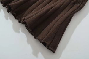 Detail of dark brown ribbed knit hem with decorative lettuce edge on pleated dress