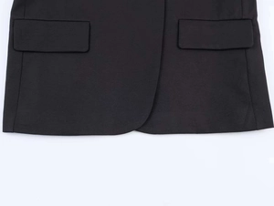 Detail view of the rounded hem and flap pockets on a black tailored blazer jacket