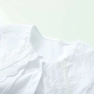 Détail d'un chemisier blanc en coton avec broderie florale et col orné de dentelle délicate