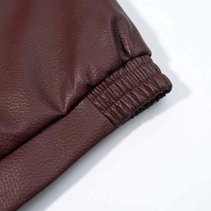 Detailed macro shot of the burgundy faux leather bomber jacket's elastic ribbed hem stitching
