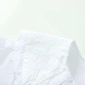 Détail de broderies florales blanches et de dentelle sur une chemise en coton