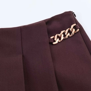 Dettaglio degli shorts a vita alta bordeaux con catena dorata e cerniera invisibile