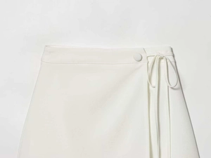 Detail of white wrap skirt with waist button closure and side ribbon tie fastening