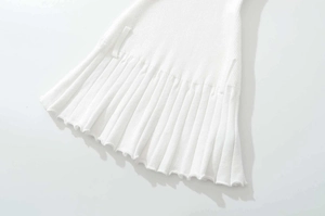 Detailed close-up of white knit dress featuring ribbed texture and pleated hemline finish
