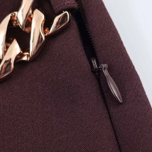 Dettaglio della cerniera di un pantaloncino con catena decorativa in metallo oro rosa