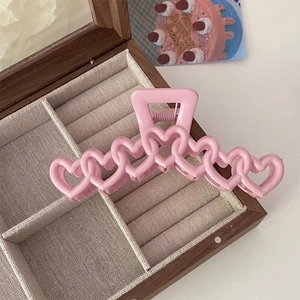 Vue détaillée d'une pince à cheveux rose en forme de cœur sur un support en bois