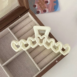 Détail d'une pince à cheveux mate ivoire en forme de cœur sur une boîte à bijoux en bois
