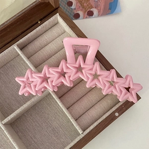 Pince à cheveux rose avec sept étoiles creuses posée sur un coffret à bijoux