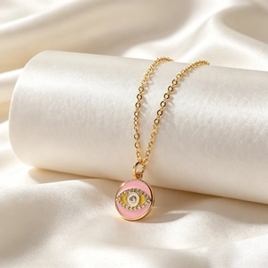 Macro shot of gold necklace featuring a pink enamel Evil Eye pendant with clear zircons
