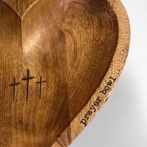 Close-up of heart-shaped wooden prayer bowl with engraved crosses and natural wood grain