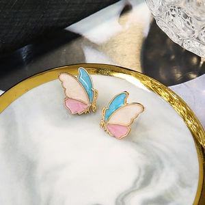 Elegant butterfly enamel earrings with pink and blue wings on a gold marble tray