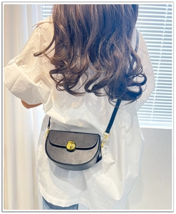 Close-up of a black leather saddle bag with gold metal buckle on a white shirt