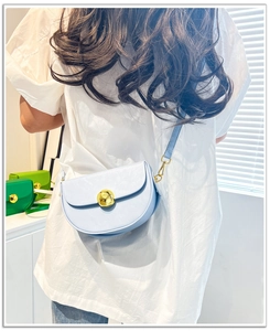 Close-up of a light blue saddle bag with a large golden spherical buckle and slim strap