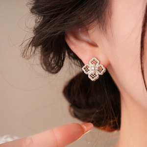 Close-up of a gold filigree clover earring with white zircons and a pearl on an ear