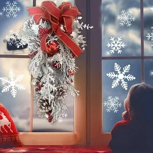 Detail of flocked Christmas teardrop wreath with red bow, pine cones, and berries on a window