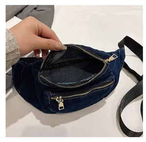 Detail view of denim waist bag showing spacious inner compartment and golden zippers