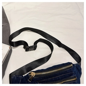 Detail view of denim waist bag showing dark blue fabric and gold metal zippers