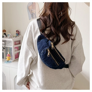 Detail of blue denim crossbody bag featuring golden zippers and adjustable nylon strap