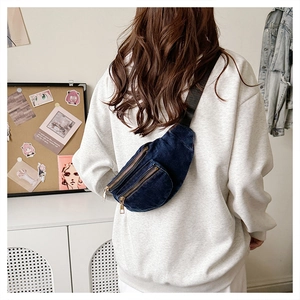 Detail of blue denim waist bag showing dual metal zippers and adjustable strap on model