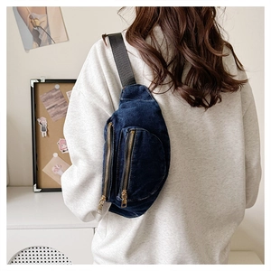 Detail of dark blue denim chest bag showing dual zippers and adjustable strap on a model