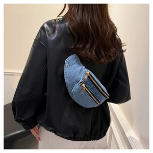 Detail of blue denim waist bag featuring double gold metal zippers and crescent shape