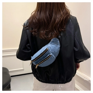 Detailed view of a blue denim crossbody chest bag with golden zippers worn over a leather jacket