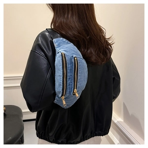 Detail of blue denim fanny pack with dual golden zippers worn over a black leather jacket