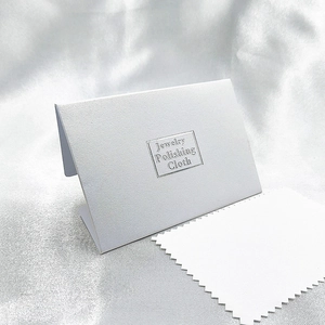 White jewelry polishing cloth with jagged edges and elegant pearlescent paper packaging