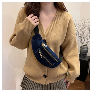 Detail of dark blue denim chest bag with gold zippers and adjustable nylon strap on model