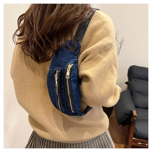 Detail of dark blue denim chest bag with dual gold zippers worn as a crossbody pack