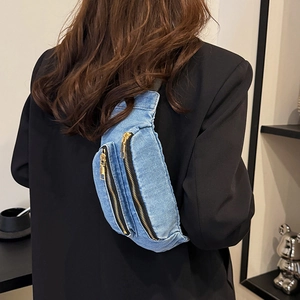 Minimalist light blue denim chest bag with gold zippers worn over a black blazer