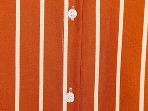 Macro detail of vertical orange and white stripes with neat white buttons on the shirt