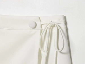 Close-up of white minimalist skirt waist featuring fabric-covered button and side tie detail