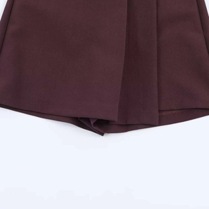 Dettaglio dei pantaloncini bordeaux a vita alta con orlo asimmetrico a pieghe e catena