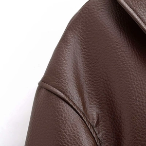 Gros plan sur la texture du cuir marron foncé et les surpiqûres de la veste vintage