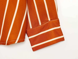 Close-up of rust orange shirt cuff with white vertical stripes and fine stitching details